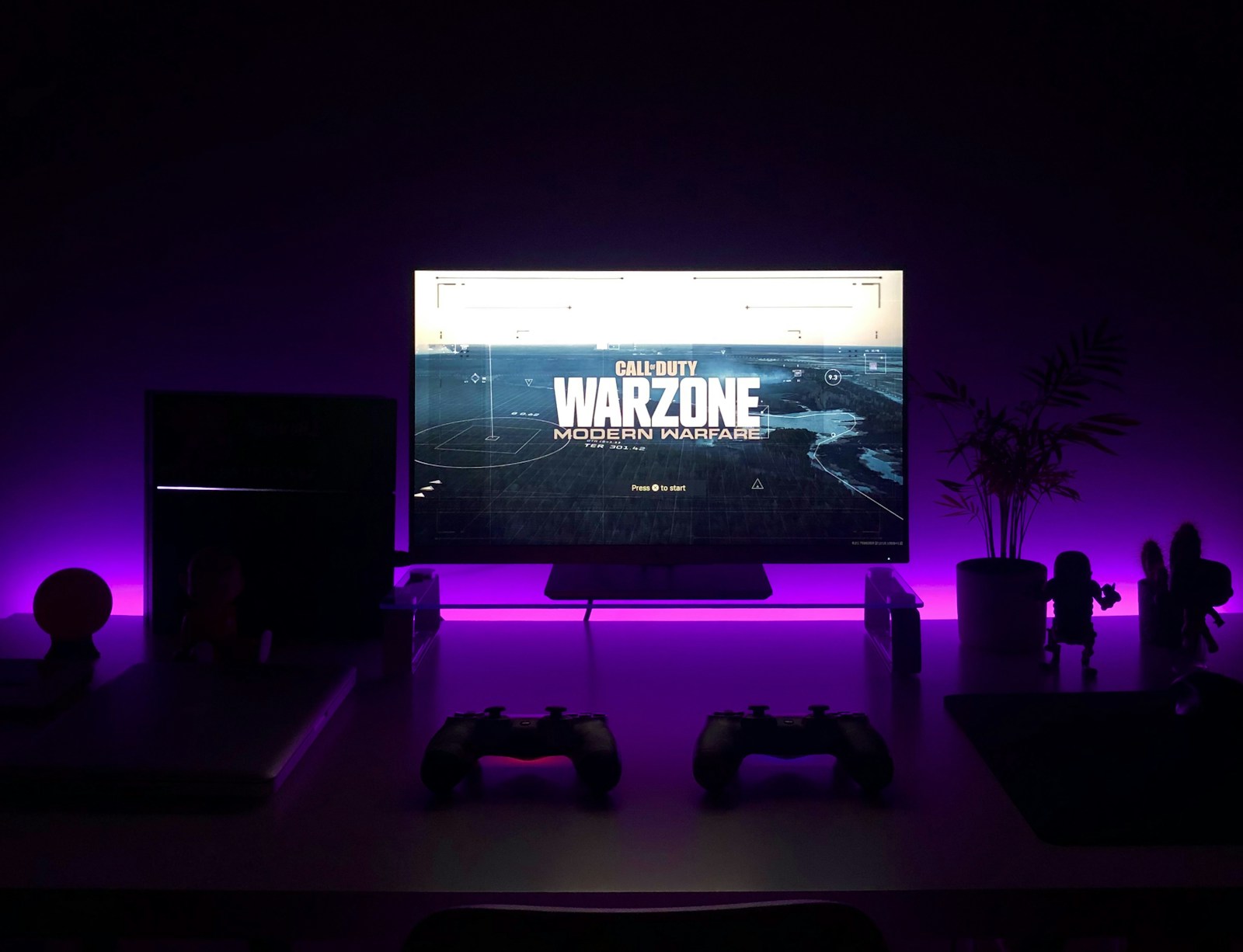 Gaming desk with a monitor, controllers, and violet accent lighting